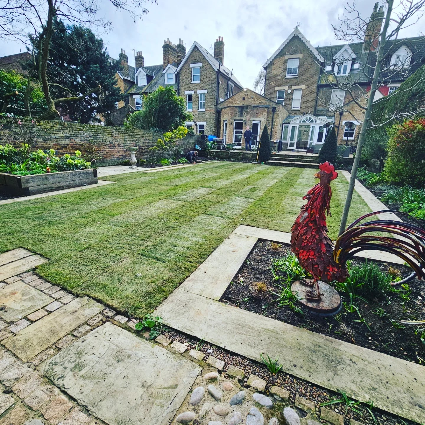 A larger formal lawn laid between stone paths in front of a period terrace — even, striped and immaculate.